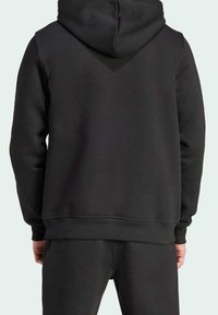 Svart luvtröja med en texturerad finish och ett V-formad designelement på baksidan, med ribbade ärmslut och nederkant.