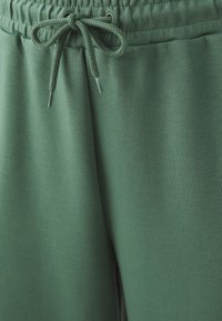 Žalios sportinės kelnės su tekstūruota medžiaga, elastinga juosmens juosta ir virvutės uždarymu su aglet detalėmis.