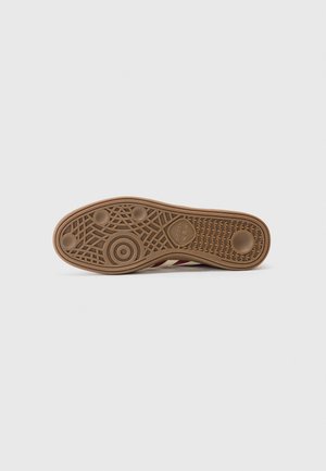 Semelle d'une chaussure Adidas marron avec des motifs circulaires, une semelle texturée et le logo Adidas Trefoil sur un fond clair uni.