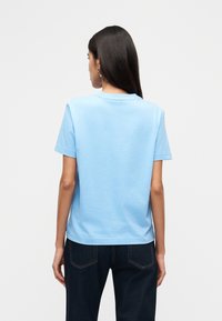 Ανοιχτό μπλε βαμβακερό μπλουζάκι με στρογγυλή λαιμόκοψη και κοντά μανίκια, με άνετη εφαρμογή και λεία υφή, εμφανιζόμενο από την πίσω πλευρά.