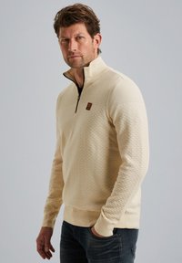 Crème-kleurige kwart-rits sweatshirt met een gestructureerd patroon, ribgebreide manchetten en een klein logo op de linkerborst.