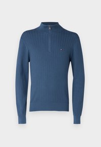 Sininen neulepusero, jossa on korkea kaulus ja puoli-vetoketju. Ominaisuuksiin kuuluu teksturoitu vinoraitakuosi ja pieni logo rinnassa.