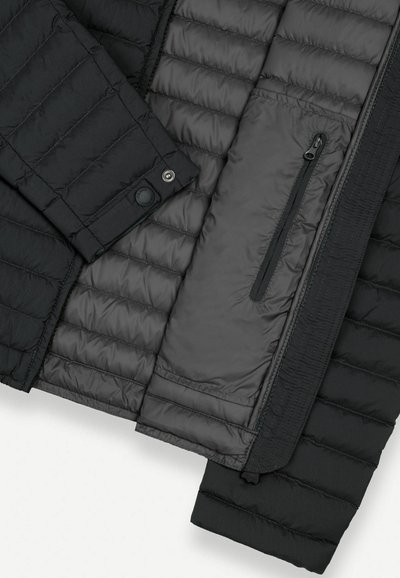 Veste matelassée noire ouverte pour montrer la poche poitrine intérieure avec fermeture éclair verticale et bouton-pression au poignet.