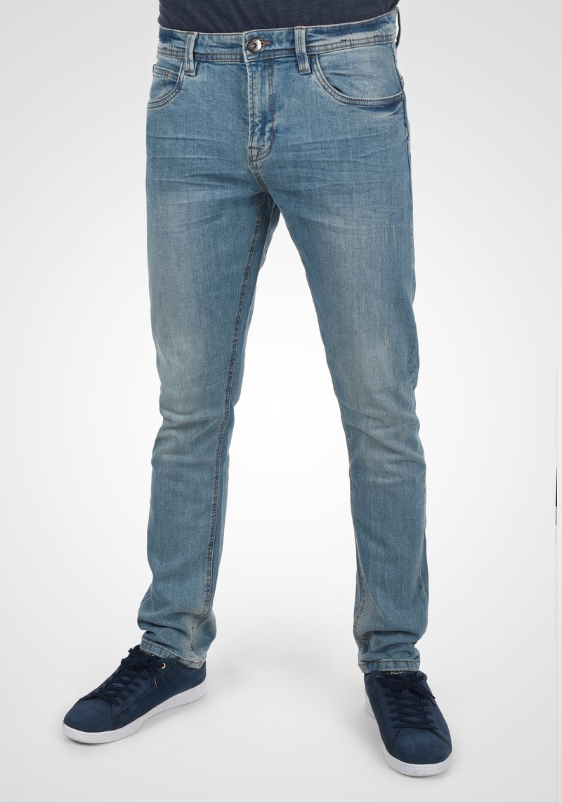 Lyseblå denimjeans med slim fit, med fem lommer, synlige sømmer og en lett falmet tekstur. Kombinert med marineblå sneakers.