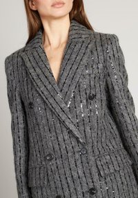 Blazer gris de doble botonadura con rayas verticales de lentejuelas negras y plateadas, tela de lana texturizada, solapas de pico y dos bolsillos frontales.