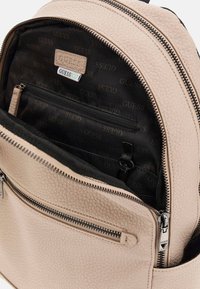 Zaino in finta pelle beige con superficie texture. Caratteristiche include una chiusura con zip, interno foderato in nero e una piccola tasca con zip per un'organizzazione ottimale.