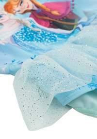 Vestito per bambino realizzato in tessuto azzurro chiaro, decorato con una stampa di due personaggi animati, completato da un sottile strato di tulle brillante.