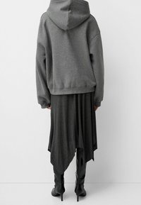 Šedá oversized mikina s jemnou texturou, spárovaná s tmavě šedými asymetrickými šaty. Černé kozačky na podpatku doplňují outfit.