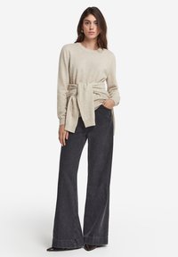 Beige stickad tröja med knut i midjan, kombinerad med vida mörka denimbyxor. Outfitsen har en avslappnad passform och mjuk textur.