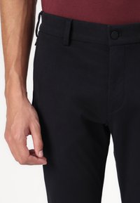 Black cotton blend trousers with a button closure, belt loops, and side pockets, featuring a smooth texture and tailored fit.
