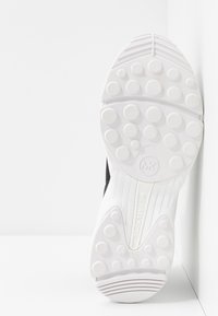 Czarny but sportowy z białą gumową podeszwą z okrągłymi bieżnikami i wytłoczonym logo. Gładka faktura z eleganckim designem.