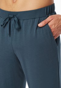 Joggers de hombre en azul oscuro, hechos de una tela suave, con una cintura acanalada y cordón ajustable, y bolsillos laterales. Textura suave y flexible.