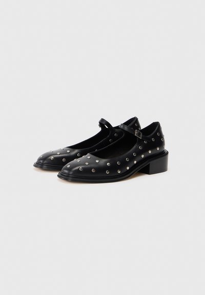 Sapatos de couro pretos com bico arredondado, tiras e salto baixo quadrado. A parte superior apresenta detalhes em prata com tachas em um design padronizado.