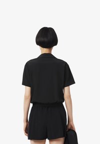 Camisa negra de manga corta con cuello, combinada con pantalones cortos negros. Tejido suave y corte relajado con cintura elástica. Sin patrones visibles.