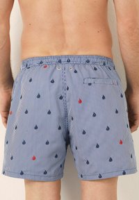 Shorts de baie bleu deschis cu dungi verticale și modele mici de velier în nuanțe de bleumarin și roșu. Brâu elastic cu un buzunar la spate și detaliu cu button.