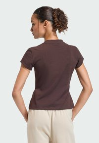 Hnedý krátky rukáv top vyrobený z mäkkej látky s priliehavým strihom a okrúhlym výstrihom. Hladká textúra a minimálne švy.