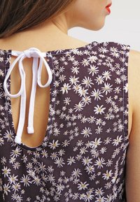 Fialový látkový top s květinovým vzorem s bílými kopretinami. Střih s výřezem na zádech, zajištěný bílou tkaničkou.