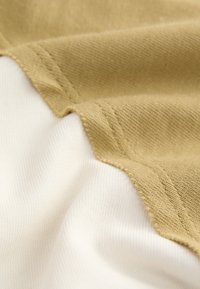 Cotton fabric with beige and white sections, featuring a textured brown surface and smooth white background, stitched at the edges.