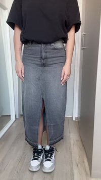 Gonna di jeans grigia scura con uno spacco frontale. Abbinata a sneakers alte bianche e argento con lacci neri. Design semplice e dritto.