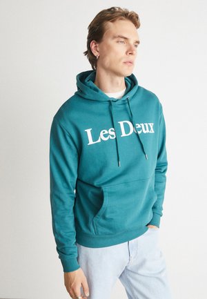 Teal pullover hoodie featuring a front kangaroo pocket, adjustable drawstrings, and white printed text "Les Deux" across the chest.