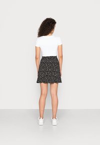 Weißes kurzärmliges Hemd kombiniert mit einem schwarzen Rock mit Polka-Dots und einem ausgestellten Saum. Das Outfit wird mit weißen Sneakern abgerundet.