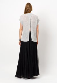 Lichtgrijze gebreide trui met korte mouwen en een split aan de achterkant, gecombineerd met een zwarte tulle maxi rok, wat gelaagde texturen creëert.
