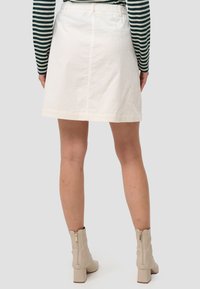 Vitt kordflamskjol i A-linje med midjeband, sydd nederkant och detaljerad bakseam, kombinerad med beige blockklackade ankelskor.