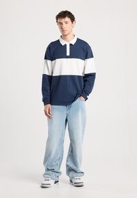 Navy and white striped long-sleeve polo with a collared neckline, paired with light blue baggy jeans and white sneakers with gray accents.