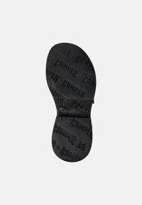 Černá gumová podešev boty s vyvýšeným vzorem loga "CAMPER" a kulatým detailem loga blízko středu. Plochý a strukturovaný design povrchu.