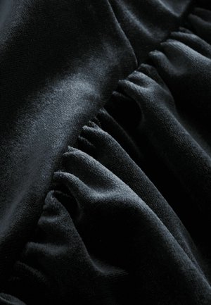 Svart sammetsliknande tyg med en slät yta och mjuk struktur, prydd med vevda veck längs en kant för ökad dimension.