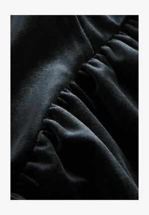 Tessuto di velluto nero con una superficie liscia e una consistenza morbida, caratterizzato da pieghe arricciate lungo un bordo per una maggiore dimensione.