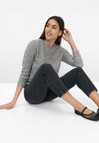 Pull en maille gris avec un col rond, associé à un jean en denim foncé. Les chaussures présentent un design en maille noire. Tenue simple et décontractée.