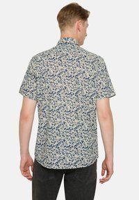 Camisa de manga corta con un patrón botánico en azul marino y crema, con dobladillo recto y cuello abotonado. Tejido de algodón.