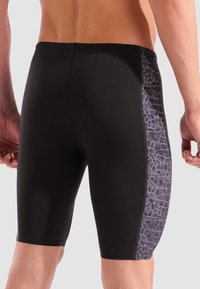 Schwarze Schwimmshorts mit einem figurbetonten Design, das ein strukturiertes graues Seitenpaneel mit einem geometrischen Muster aufweist. Glatter Stoff, mittellange Hosenlänge bis zur Oberschenke.