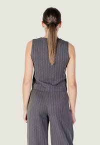 Top smanicato grigio a righe sottili abbinato a pantaloni a gamba larga coordinati, con una texture liscia e una lieve lucentezza. Il design presenta righe verticali.