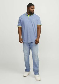 Short-sleeved blue polo shirt with neon green collar and sleeve accents, worn with light wash denim jeans and white sneakers.