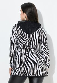 Schwarz-weiß gestreifter Kapuzenpullover mit langen Ärmeln, aus weichem Stoff gefertigt, mit einer Kapuze aus schwarzem Netz und einer lässigen Passform.