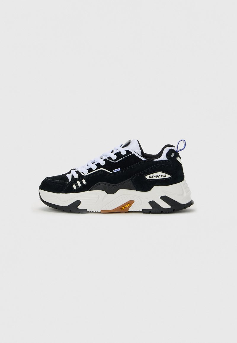 Black and white low-top sneaker with thick sole, white laces, and branding details on side, against a plain light background.