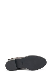Zapato de cuero marrón con un diseño texturizado, punta cerrada y suela de goma sólida. La suela es plana con una ligera curva en la punta.