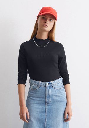 Zwart geribbelde long-sleeve top met geschulpte halslijn, gecombineerd met een lichtblauwe denimrok. Een levendige rode pet maakt de outfit compleet.