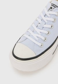 Light blue canvas sneaker with white laces, silver eyelets, and a round white rubber toe cap. Features a black rubber sole accent.