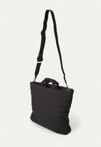 Black padded tote bag with adjustable strap and dual top handles. Textured fabric features horizontal pleats and a soft finish.