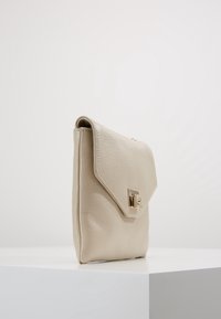 Vaaleanbeige nahkainen käsilaukku, jossa on rakenteellinen pinta, kolmion muotoinen läppä ja kultasävytteiset yksityiskohdat. Varustettu turvallisella lukolla ja kompaktilla suorakulmaisella muodolla.