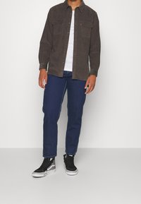Donkergrijs overhemdd met twee borstzakken, gecombineerd met blauwe jeans en zwarte hoge sneakers met witte accenten.