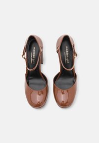 Bruna lackläderklackar med rund tå, ankelsnörning och detaljer i guld. Svart innerfoder. Solid färg, slät textur.