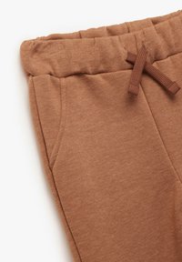 Pantalon de survêtement en coton brun avec une taille élastique, un cordon de serrage et des poches latérales. Texture douce et coupe décontractée.