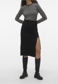 Czarna i biała w paski koszula z długim rękawem o okrągłym dekolcie zestawiona z dopasowaną czarną spódnicą z bocznym rozcięciem, noszona z wysokimi czarnymi botkami do kolan.