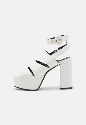 White platform sandals with a chunky block heel, featuring multiple horizontal straps and an ankle strap with a circular buckle detail.