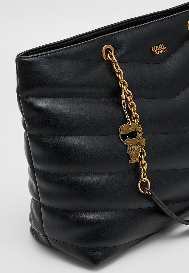 Bolso tote negro acolchado de cuero, con herrajes dorados y un llavero decorativo. Textura lisa con patrones de costuras distintivos.