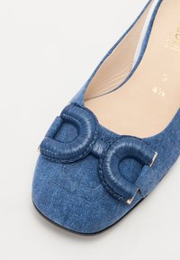 Chaussure plate en denim bleu avec bout carré arrondi et grand nœud tressé bleu décoratif sur le dessus.
